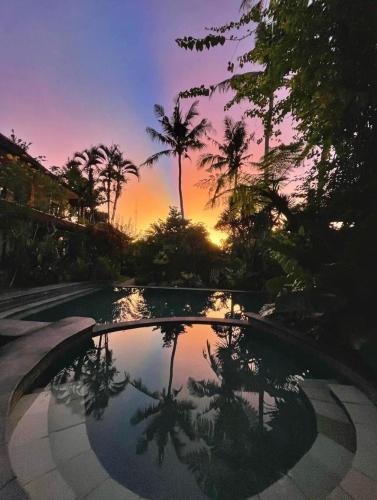 a pool with palm trees and a sunset in the background at White House in Ubud