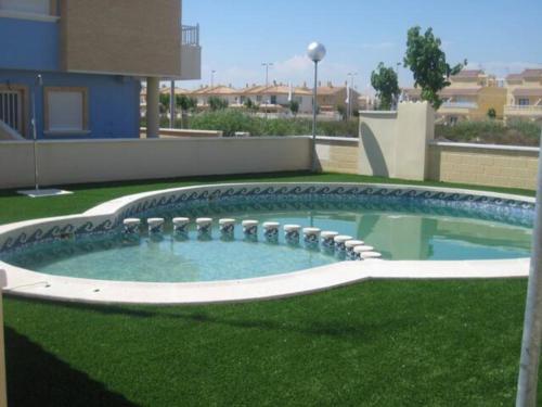 uma piscina num quintal com relva verde em Bungalow planta baja con amplia terraza 120m2 residencial privado con piscina em Pilar de la Horadada