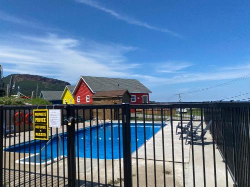 a swimming pool behind a fence in front of a house at Hotel-Motel Le Panorama in Perce