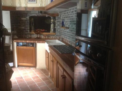 une cuisine avec des placards en bois et un mur en briques dans l'établissement Les cigales gîte cigalou, à Grospierres