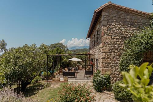 ein Steingebäude mit einer Terrasse mit einem Sonnenschirm in der Unterkunft Casa Rural en Candeleda con piscina y un maravilloso jardín in Candeleda