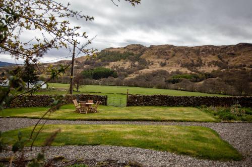 a table and chairs in a yard with mountains in the background at Kennels Cottage in Killin