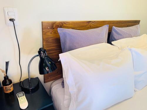 a bed with white sheets and a table with a phone on it at Maritimus Suites Apartamento 07 in Barretos