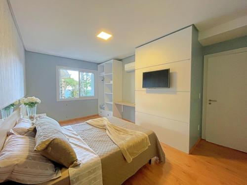 ein Schlafzimmer mit einem Bett und einem Fernseher an der Wand in der Unterkunft Espaçoso apto no Centro de Gramado in Gramado
