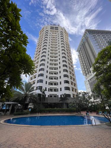 a large white building with a pool in front of it at Grand Diamond Condo Suites in Bangkok