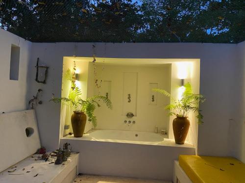 a bathroom with a tub with two plants and a mirror at Manta Cottage - Forest view in Galu