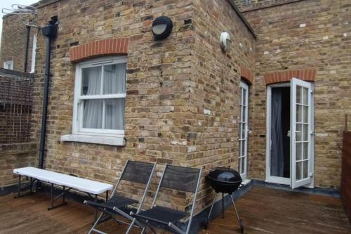 a grill and two chairs on a patio next to a brick building at Quiet and cozy 2 SEPERATE BEDROOMS and 2 BATHROOM with terrace in London