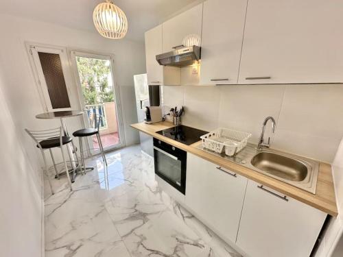 La cuisine est équipée de placards blancs, d'un évier et d'un comptoir. dans l'établissement Superbe appartement neuf - Plage à 5 min à pied, à Nice