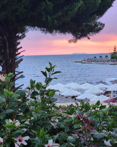 a beach with white umbrellas and the ocean at sunset at Amelie's Apartments & Beach Saranda in Sarandë