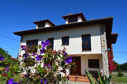 Uma casa branca com flores roxas à frente. em Villa El Martín em Naves