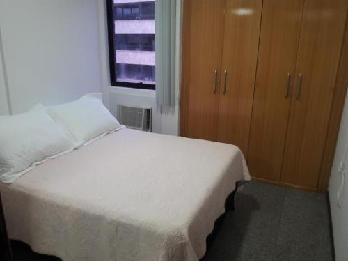 een slaapkamer met een wit bed en houten kasten bij Excelente quarto/sala in Maceió