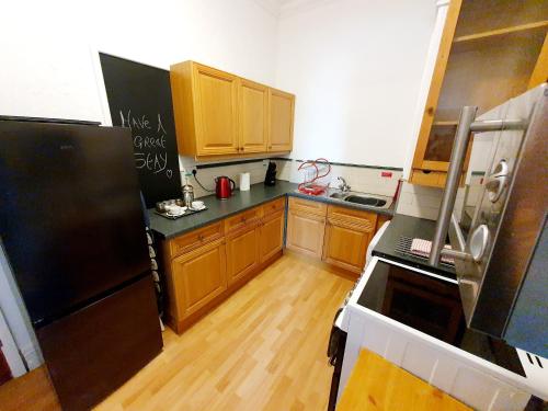 a kitchen with a black refrigerator and wooden cabinets at F3 2 BEDROOMED TOWN HOUSE - FREE Parking - Super 150 Mbps WiFi Near Gavin n Stacey Film House - 1 FREE DOG ALLOWED in Barry