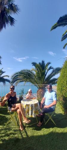 drie mensen aan een tafel met de oceaan op de achtergrond bij Villa Panoramica in Menton