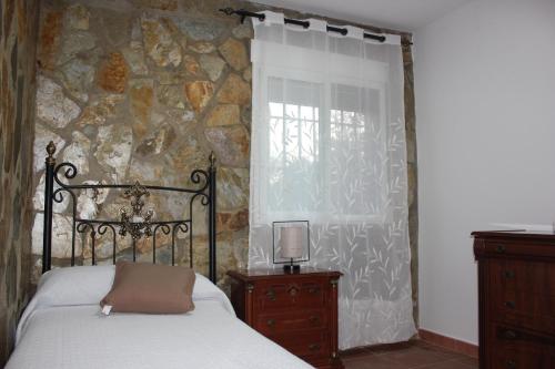 1 dormitorio con cama y pared de piedra en Casa Vacacional El Cañizo en Córdoba