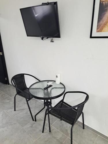 a glass table with two chairs and a television on a wall at Blanco Sereno - Depto 2 - 2 Min Malecón in Mazatlán