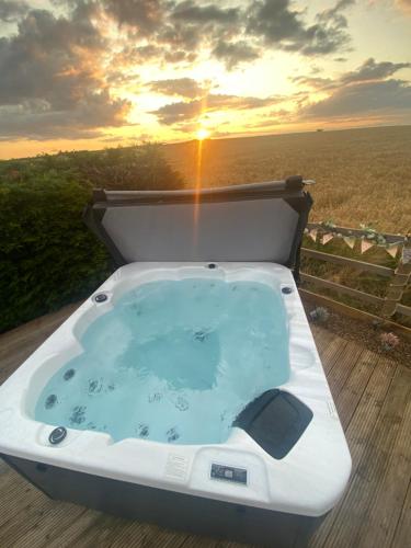 a bath tub on a deck with the sunset in the background at Country Bumpkins Luxury Glamping in Wellingore
