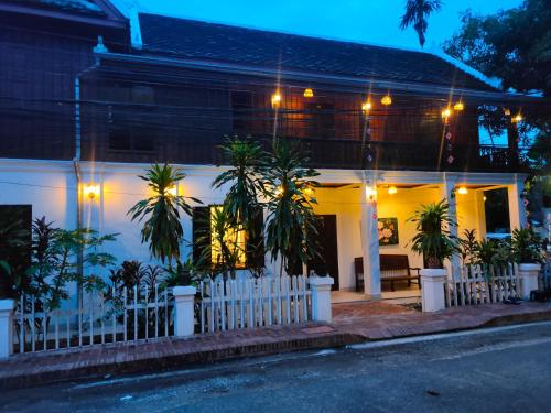 a white house with a fence and palm trees at Lotus Corner - Vegan & Plant Based B&B in Luang Prabang