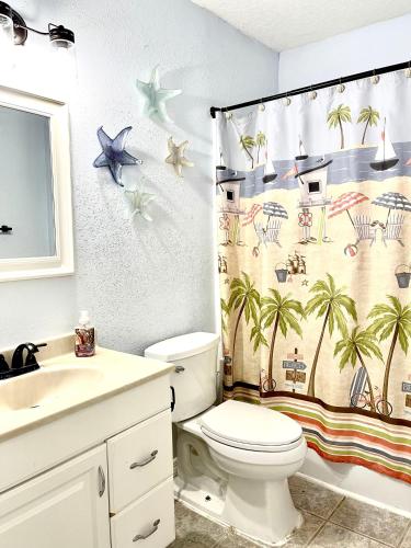 La salle de bains est pourvue de toilettes et d'un rideau de douche avec des palmiers. dans l'établissement A Cozy Space Coast Retreat, à Titusville