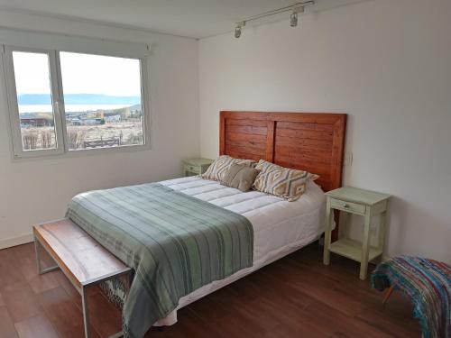 エル・カラファテにあるCasa Glaciar Patagoniaのベッドルーム1室(木製ヘッドボード付きのベッド1台、窓2つ付)