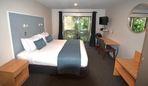 a bedroom with a bed and a desk and a window at La Rochelle Motel in Akaroa