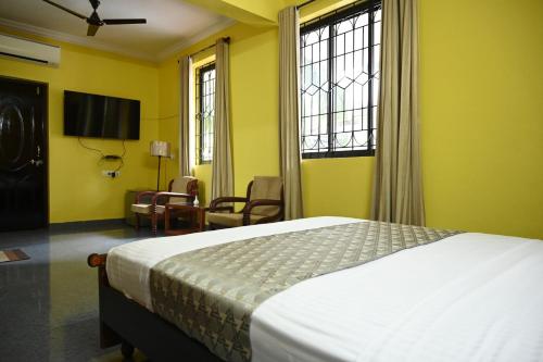 a bedroom with a bed and a chair and windows at Hotel Siesta De Goa in Varca