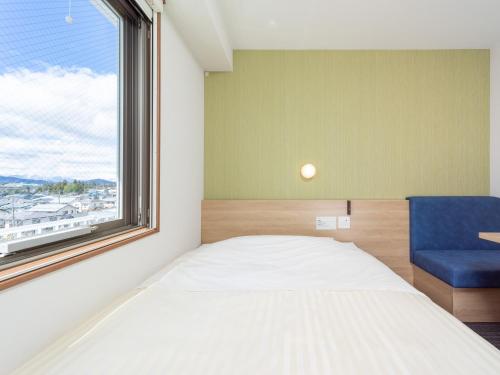 a bedroom with a bed and a window and a blue chair at Super Hotel Yahaba Station East Exit in Yahaba