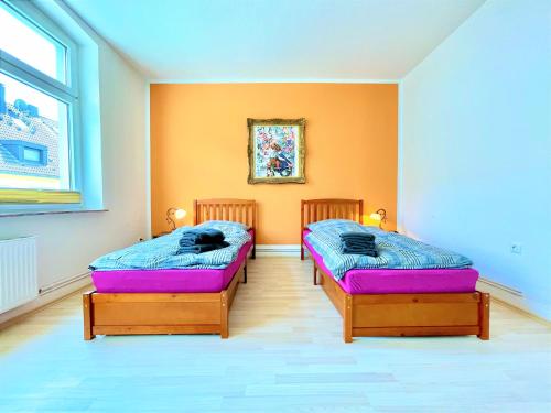 2 Betten in einem Zimmer mit orangefarbener Wand in der Unterkunft Betongold in Duisburg