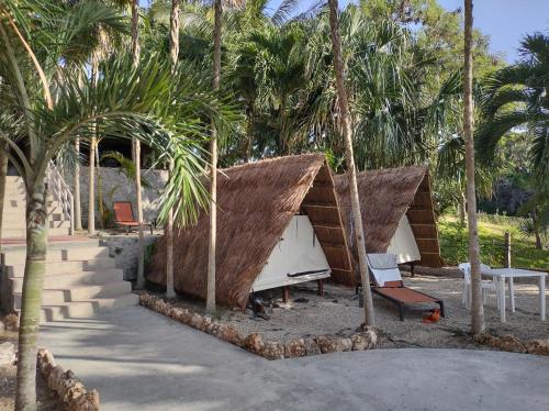 a couple of huts with palm trees and a table at Glamping Asana Bacalar in Bacalar