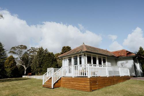 une maison blanche avec une terrasse couverte sur la pelouse dans l'établissement Mount Booralee, à Blackheath