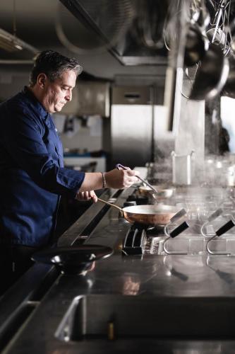 a man in a kitchen preparing food in a wok at Hotel Ladinia in La Villa