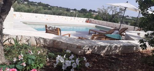 a pool with chairs and an umbrella next to a stone wall at Holiday Home Cosimo in Locorotondo