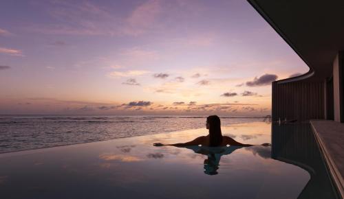 a woman sitting in a infinity pool looking at the ocean at The Ritz-Carlton Maldives, Fari Islands in North Male Atoll