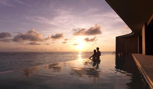 a man and woman standing in a infinity pool overlooking the ocean at The Ritz-Carlton Maldives, Fari Islands in North Male Atoll