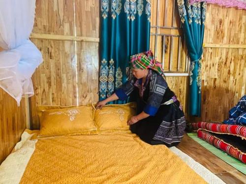 una mujer sentada junto a una cama en una habitación en Homestay Ngọc Thủy Điểm dừng chân lên Đồi Mâm Xôi en Mù Cang Chải