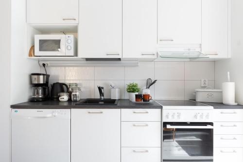 a white kitchen with white cabinets and a microwave at Cosy studio apartment + free private parking in Kangasala