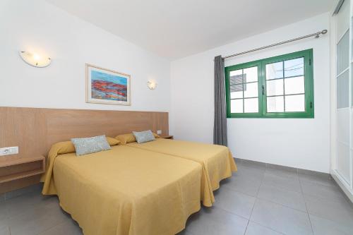 a bedroom with a bed with a yellow bedspread and a window at Apartamentos Elena in Puerto del Carmen