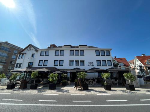 a white building with tables and umbrellas on a street at Hotel Azur in De Haan