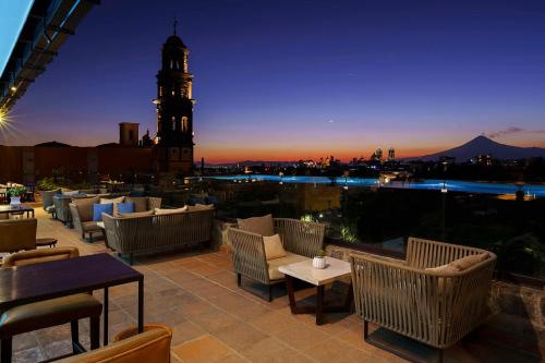 eine Dachterrasse mit Stühlen und einem Uhrturm in der Nacht in der Unterkunft Banyan Tree Puebla in Puebla