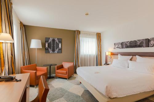 a hotel room with a bed and a desk and chairs at Holiday Inn Mulhouse by IHG in Mulhouse