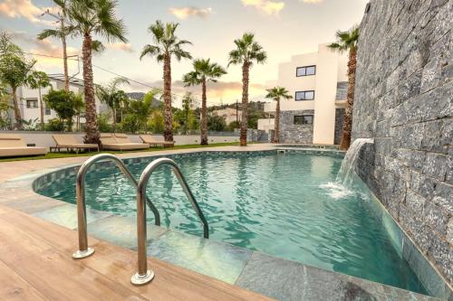 a swimming pool with a waterfall and palm trees at Lazar Lux Suites - Ammoudara in Agios Nikolaos