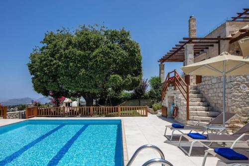 a pool with chairs and an umbrella and a house at Villa Eleftherna in Elefterna