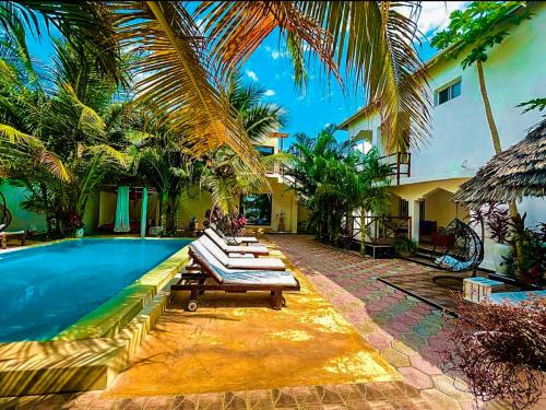 - une piscine avec des chaises longues et des palmiers à côté d'une maison dans l'établissement CeZeRe THE PALM HOTEL, à Paje