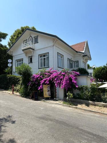 Uma casa branca com flores roxas à frente. em Serguzest Otel em Buyukada