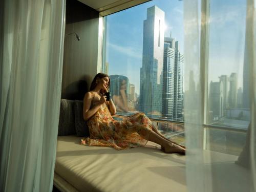 a woman sitting on a window sill talking on a cell phone at Towers Rotana - Dubai in Dubai