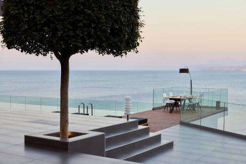 a table and a tree on a balcony with the ocean at Beachfront Villa in Crete - Epavli Luxury Villa in Agia Pelagia