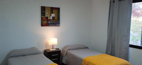 Un dormitorio con dos camas y una lámpara y una ventana. en Casa Ton Trevelin, en Trevelín