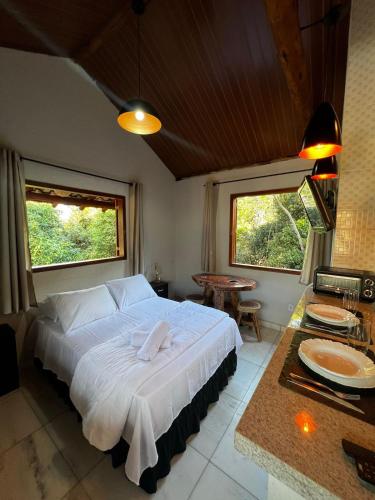 a bedroom with a large white bed and a table at Cantinhos do Cipó - Chales privativos com hidro in Serra do Cipo