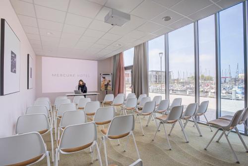 a room with white chairs and a woman standing in a room with windows at Mercure Dunkerque Centre Gare in Dunkerque