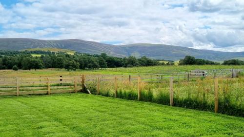 a fence in a field with mountains in the background at Bombie Glamping Pod in Grantown on Spey