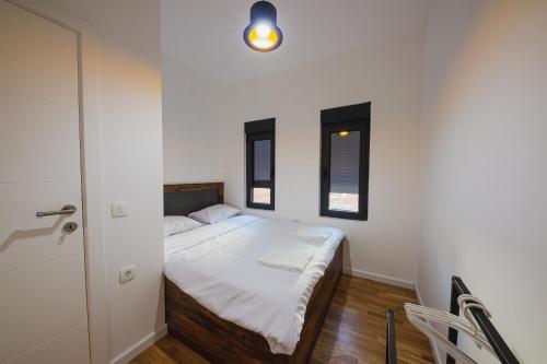 a small bedroom with a white bed and two windows at KOKO VILLAGE in Podgorica